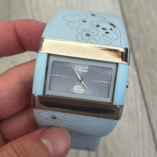 Nike WC0024-624 Merge Attract Baby Blue Digital Watch is a digital wristwatch featuring a silver-tone stainless steel case with a analog display. The straps are baby blue with engraved floral pattern graphics on the outer side and a beige inner lining, made from a combination of leather, plastic, and rubber materials. The dial is metallic baby blue with small dots pattern.