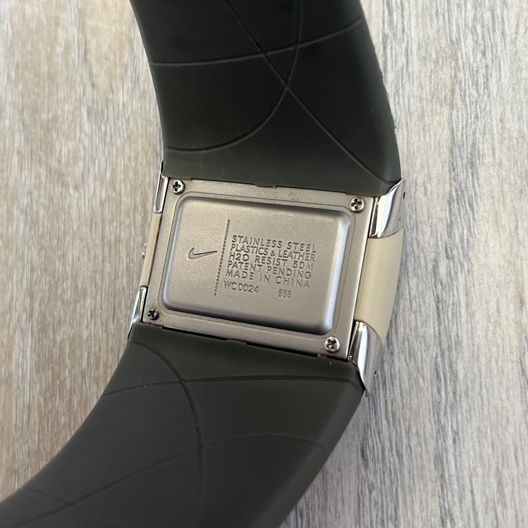 Nike WC0024-668 Merge Attract Beige Digital Watch is a digital wristwatch featuring a silver-tone stainless steel case with a analog display. The straps are beige with engraved line pattern graphics on the outer side and a dark grey inner lining, made from a combination of leather, plastic, and rubber materials. The dial is metallic beige with no numbers.
