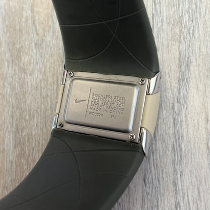 Nike WC0024-668 Merge Attract Beige Digital Watch is a digital wristwatch featuring a silver-tone stainless steel case with a analog display. The straps are beige with engraved line pattern graphics on the outer side and a dark grey inner lining, made from a combination of leather, plastic, and rubber materials. The dial is metallic beige with no numbers.
