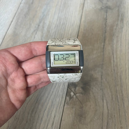 Nike WC0033 Merge Transit Digital Watch is a digital wristwatch featuring a silver-tone stainless steel case with a digital display and two gray side buttons on each side. The strap is white with engraved floral-style graphics on the outer side and a grey inner lining, made from a combination of leather, plastic, and rubber materials. The watch includes multiple modes and is water resistant up to 50 meters.
