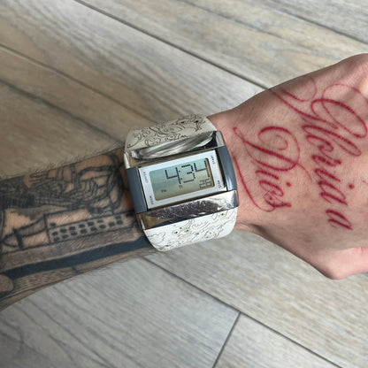 Nike WC0033 Merge Transit Digital Watch is a digital wristwatch featuring a silver-tone stainless steel case with a digital display and two gray side buttons on each side. The strap is white with engraved floral-style graphics on the outer side and a grey inner lining, made from a combination of leather, plastic, and rubber materials. The watch includes multiple modes and is water resistant up to 50 meters.
