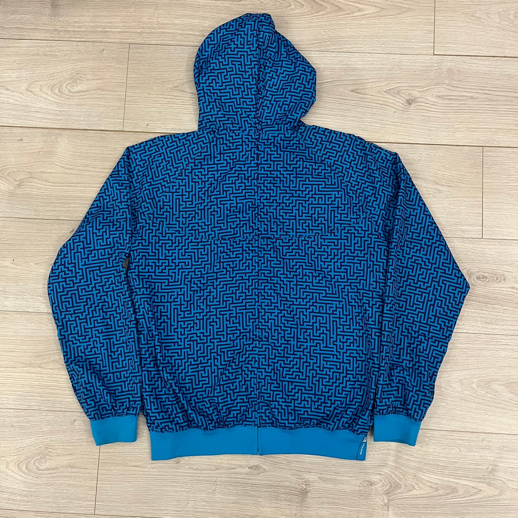 The Nike x Wood Wood “Labyrinth” Split Windbreaker (237110-400) features a full laser blue polyester body with an all-over navy labyrinth print. Designed in Copenhagen, the jacket includes zippers on the front and back allowing it to merge with other compatible models, an embroidered Nike logo and a subtle Wood Wood tag. Inside, a unique printed message from the Wood Wood founders references the jacket’s “Labyrinth” inspiration.