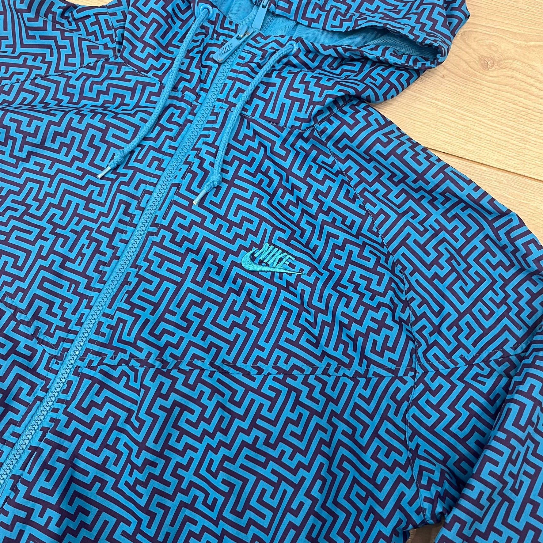 The Nike x Wood Wood “Labyrinth” Split Windbreaker (237110-400) features a full laser blue polyester body with an all-over navy labyrinth print. Designed in Copenhagen, the jacket includes zippers on the front and back allowing it to merge with other compatible models, an embroidered Nike logo and a subtle Wood Wood tag. Inside, a unique printed message from the Wood Wood founders references the jacket’s “Labyrinth” inspiration.