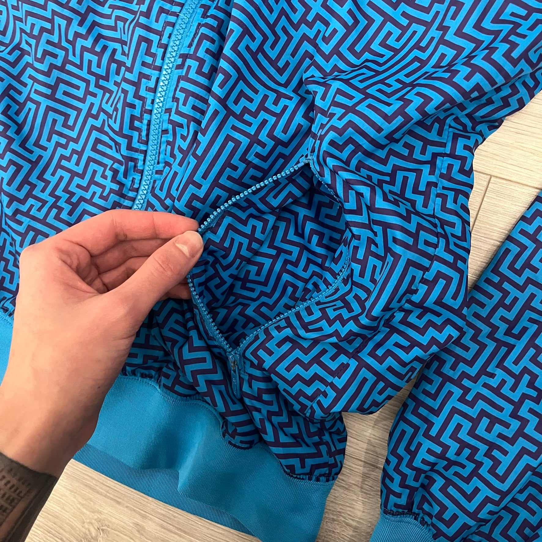 The Nike x Wood Wood “Labyrinth” Split Windbreaker (237110-400) features a full laser blue polyester body with an all-over navy labyrinth print. Designed in Copenhagen, the jacket includes zippers on the front and back allowing it to merge with other compatible models, an embroidered Nike logo and a subtle Wood Wood tag. Inside, a unique printed message from the Wood Wood founders references the jacket’s “Labyrinth” inspiration.