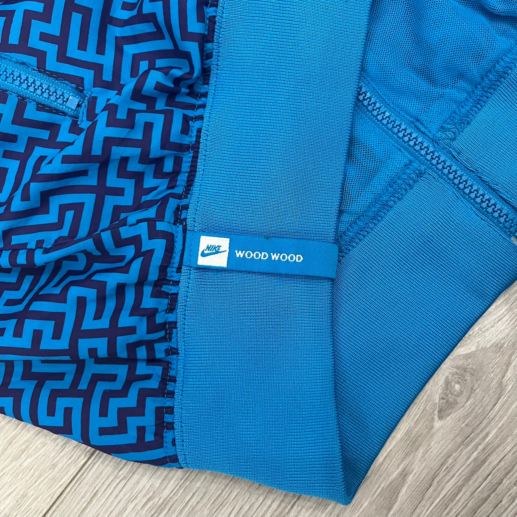 The Nike x Wood Wood “Labyrinth” Split Windbreaker (237110-400) features a full laser blue polyester body with an all-over navy labyrinth print. Designed in Copenhagen, the jacket includes zippers on the front and back allowing it to merge with other compatible models, an embroidered Nike logo and a subtle Wood Wood tag. Inside, a unique printed message from the Wood Wood founders references the jacket’s “Labyrinth” inspiration.