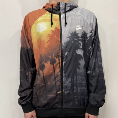 This Nike “Beach Sunset” Split Windbreaker merges two distinct colorways into one. Created from dual jackets that zip together through the front and back. The all-over print features palms, clouds, and a vibrant sunset, with one side in yellow–orange tones and the opposite in grey with black palm silhouettes. A minimal white Swoosh embroidery adds the final touch to this rare and highly collectible windbreaker.