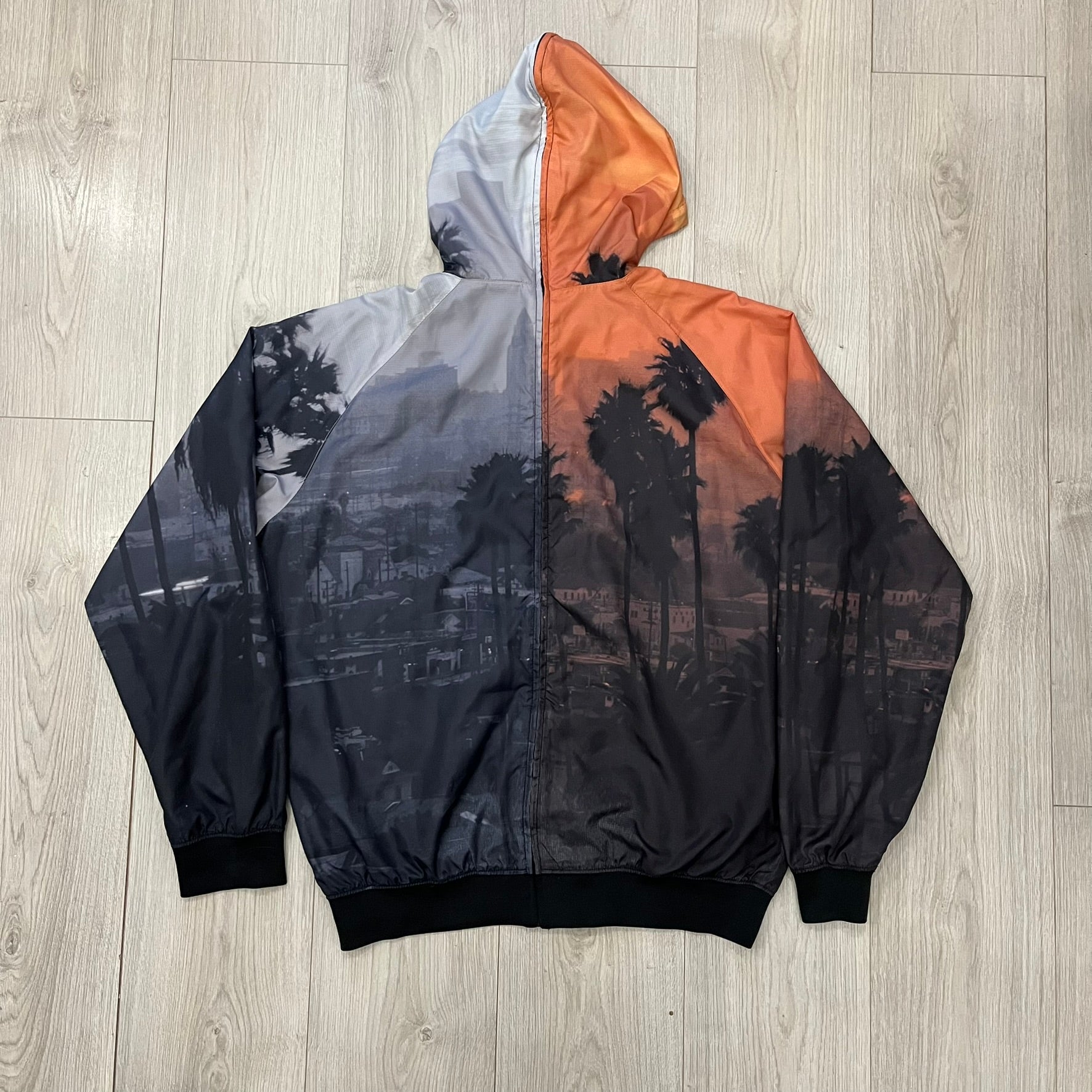 This Nike “Beach Sunset” Split Windbreaker merges two distinct colorways into one. Created from dual jackets that zip together through the front and back. The all-over print features palms, clouds, and a vibrant sunset, with one side in yellow–orange tones and the opposite in grey with black palm silhouettes. A minimal white Swoosh embroidery adds the final touch to this rare and highly collectible windbreaker.