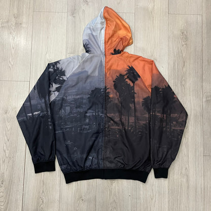 This Nike “Beach Sunset” Split Windbreaker merges two distinct colorways into one. Created from dual jackets that zip together through the front and back. The all-over print features palms, clouds, and a vibrant sunset, with one side in yellow–orange tones and the opposite in grey with black palm silhouettes. A minimal white Swoosh embroidery adds the final touch to this rare and highly collectible windbreaker.