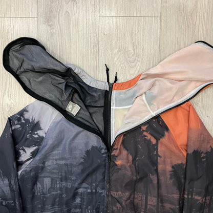 This Nike “Beach Sunset” Split Windbreaker merges two distinct colorways into one. Created from dual jackets that zip together through the front and back. The all-over print features palms, clouds, and a vibrant sunset, with one side in yellow–orange tones and the opposite in grey with black palm silhouettes. A minimal white Swoosh embroidery adds the final touch to this rare and highly collectible windbreaker.