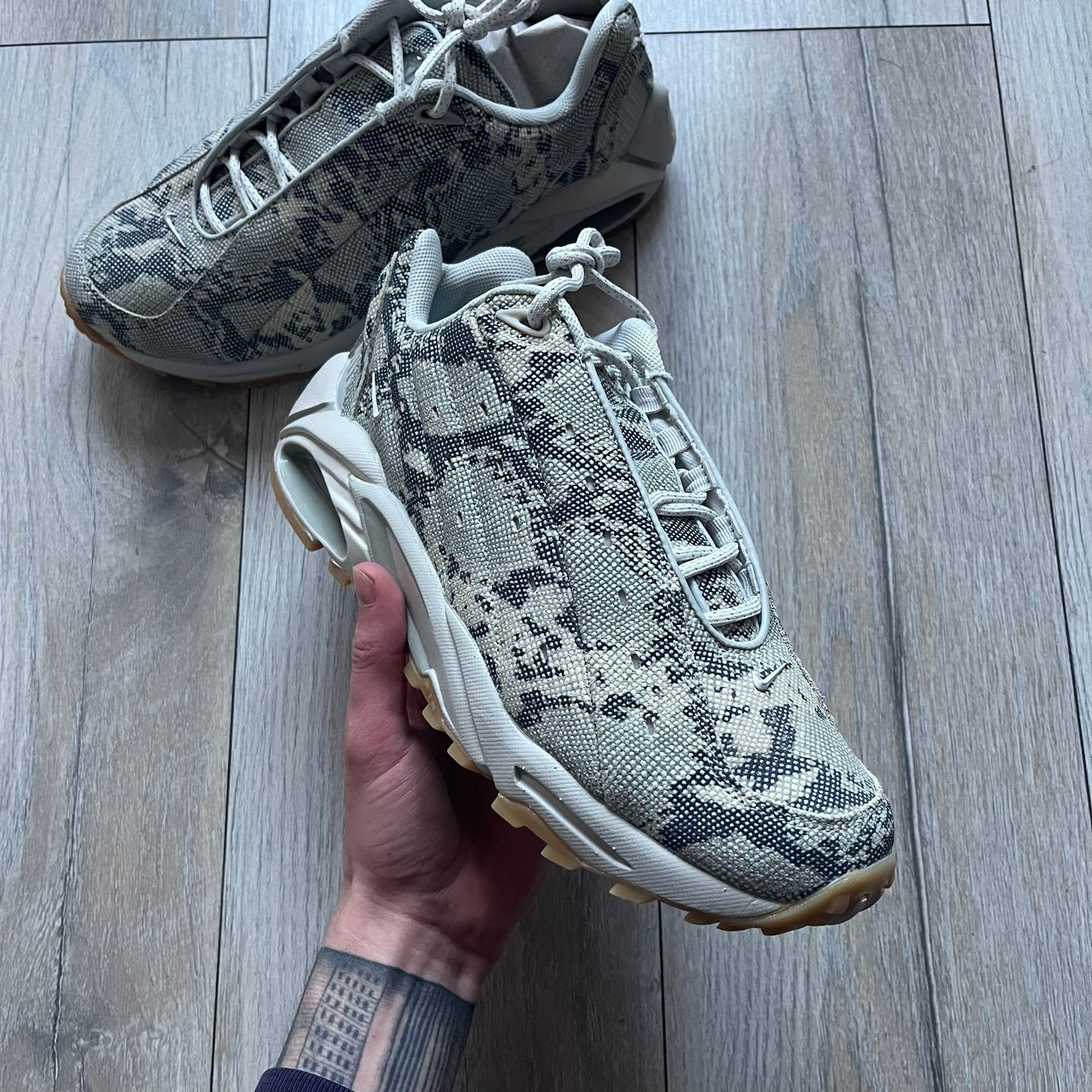 The Nike x NOCTA Hot Step Air Terra “Snakeskin” Light Bone Sneakers feature a low-top silhouette with a textured faux snakeskin upper in Light Bone tones mixed with cobblestone and gum light brown accents. The shoe includes small Swoosh logos on the sides, NOCTA three-star branding on the tongue, perforated quarter panels, and a metallic heel tag with Gore-Tex embossing. Finished with a white midsole housing a visible Air unit at the heel and a gum rubber outsole, style code DR0508-001, colorway Light Bone/