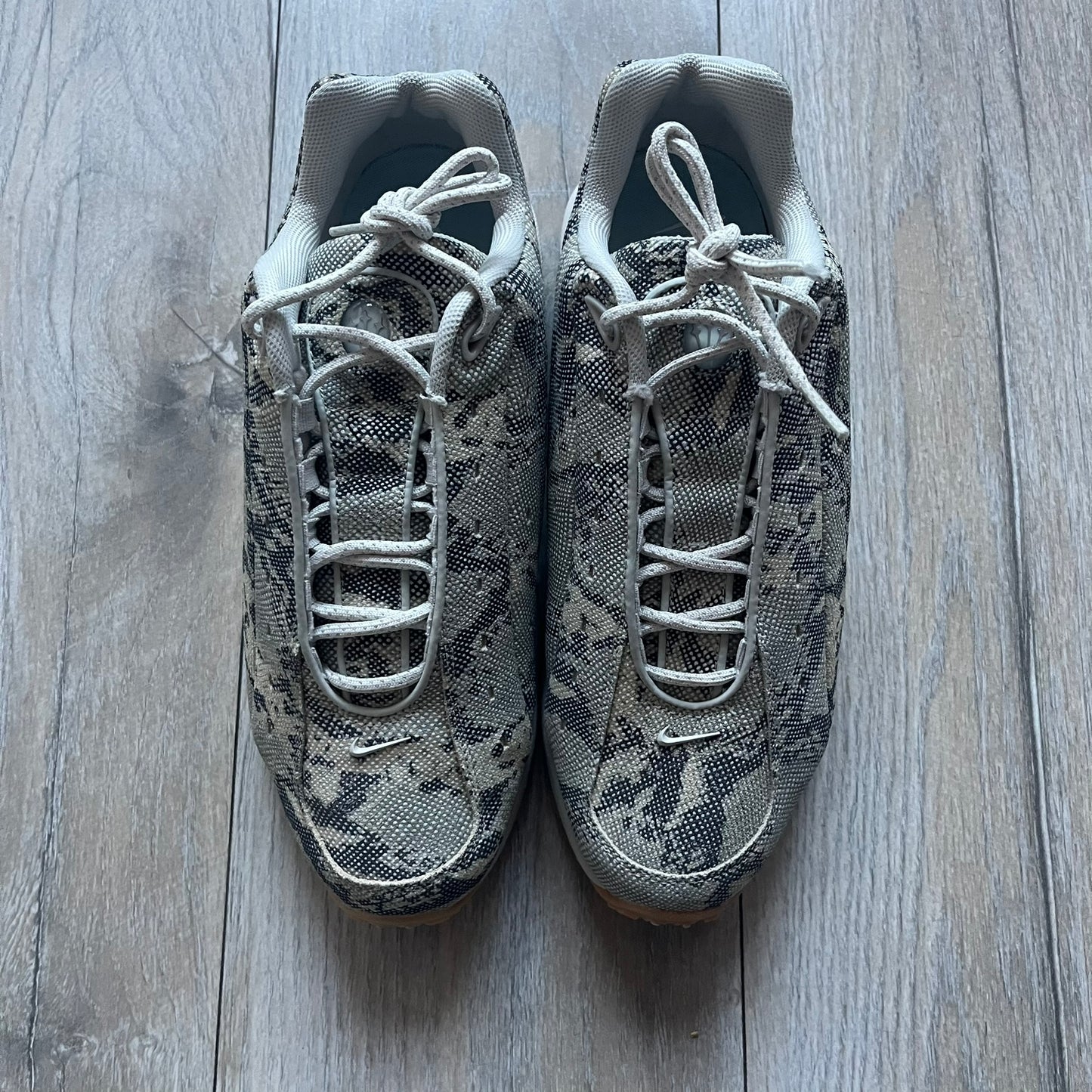 The Nike x NOCTA Hot Step Air Terra “Snakeskin” Light Bone Sneakers feature a low-top silhouette with a textured faux snakeskin upper in Light Bone tones mixed with cobblestone and gum light brown accents. The shoe includes small Swoosh logos on the sides, NOCTA three-star branding on the tongue, perforated quarter panels, and a metallic heel tag with Gore-Tex embossing. Finished with a white midsole housing a visible Air unit at the heel and a gum rubber outsole, style code DR0508-001, colorway Light Bone/