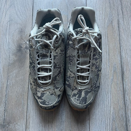 The Nike x NOCTA Hot Step Air Terra “Snakeskin” Light Bone Sneakers feature a low-top silhouette with a textured faux snakeskin upper in Light Bone tones mixed with cobblestone and gum light brown accents. The shoe includes small Swoosh logos on the sides, NOCTA three-star branding on the tongue, perforated quarter panels, and a metallic heel tag with Gore-Tex embossing. Finished with a white midsole housing a visible Air unit at the heel and a gum rubber outsole, style code DR0508-001, colorway Light Bone/