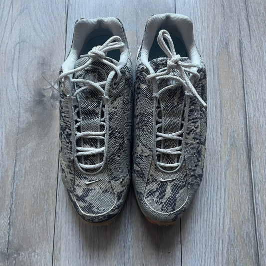 The Nike x NOCTA Hot Step Air Terra “Snakeskin” Light Bone Sneakers feature a low-top silhouette with a textured faux snakeskin upper in Light Bone tones mixed with cobblestone and gum light brown accents. The shoe includes small Swoosh logos on the sides, NOCTA three-star branding on the tongue, perforated quarter panels, and a metallic heel tag with Gore-Tex embossing. Finished with a white midsole housing a visible Air unit at the heel and a gum rubber outsole, style code DR0508-001, colorway Light Bone/