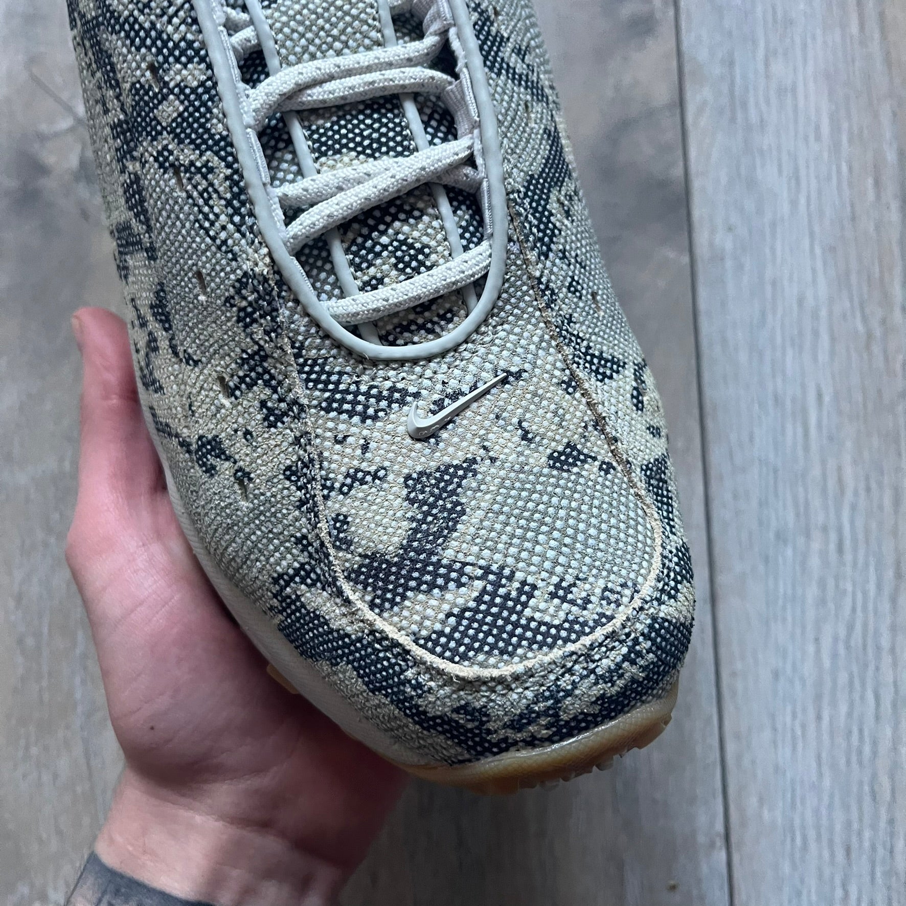 The Nike x NOCTA Hot Step Air Terra “Snakeskin” Light Bone Sneakers feature a low-top silhouette with a textured faux snakeskin upper in Light Bone tones mixed with cobblestone and gum light brown accents. The shoe includes small Swoosh logos on the sides, NOCTA three-star branding on the tongue, perforated quarter panels, and a metallic heel tag with Gore-Tex embossing. Finished with a white midsole housing a visible Air unit at the heel and a gum rubber outsole, style code DR0508-001, colorway Light Bone/