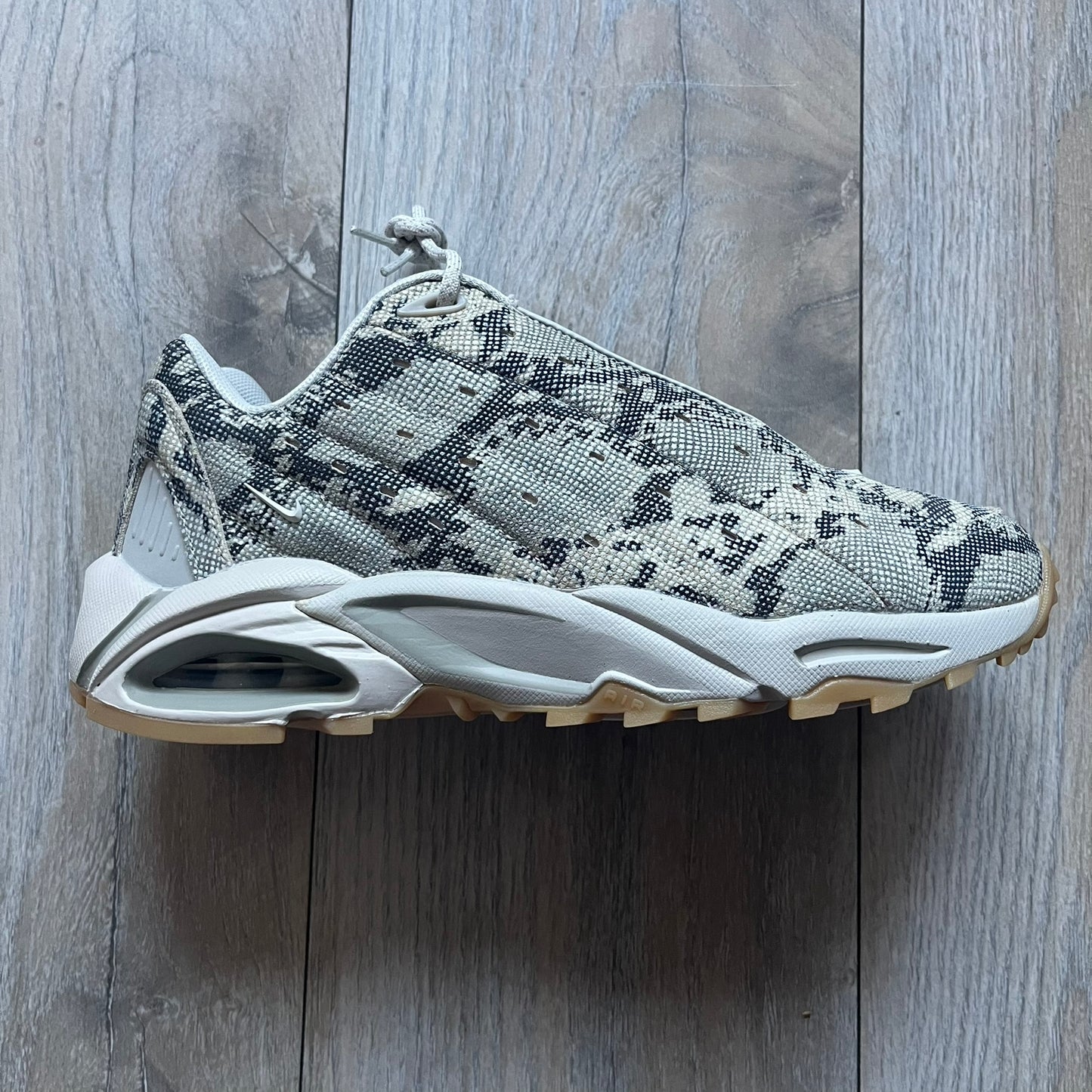 The Nike x NOCTA Hot Step Air Terra “Snakeskin” Light Bone Sneakers feature a low-top silhouette with a textured faux snakeskin upper in Light Bone tones mixed with cobblestone and gum light brown accents. The shoe includes small Swoosh logos on the sides, NOCTA three-star branding on the tongue, perforated quarter panels, and a metallic heel tag with Gore-Tex embossing. Finished with a white midsole housing a visible Air unit at the heel and a gum rubber outsole, style code DR0508-001, colorway Light Bone/