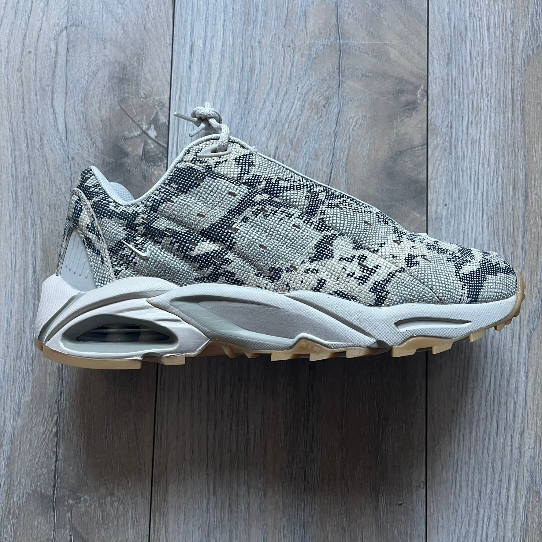 The Nike x NOCTA Hot Step Air Terra “Snakeskin” Light Bone Sneakers feature a low-top silhouette with a textured faux snakeskin upper in Light Bone tones mixed with cobblestone and gum light brown accents. The shoe includes small Swoosh logos on the sides, NOCTA three-star branding on the tongue, perforated quarter panels, and a metallic heel tag with Gore-Tex embossing. Finished with a white midsole housing a visible Air unit at the heel and a gum rubber outsole, style code DR0508-001, colorway Light Bone/