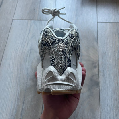 The Nike x NOCTA Hot Step Air Terra “Snakeskin” Light Bone Sneakers feature a low-top silhouette with a textured faux snakeskin upper in Light Bone tones mixed with cobblestone and gum light brown accents. The shoe includes small Swoosh logos on the sides, NOCTA three-star branding on the tongue, perforated quarter panels, and a metallic heel tag with Gore-Tex embossing. Finished with a white midsole housing a visible Air unit at the heel and a gum rubber outsole, style code DR0508-001, colorway Light Bone/