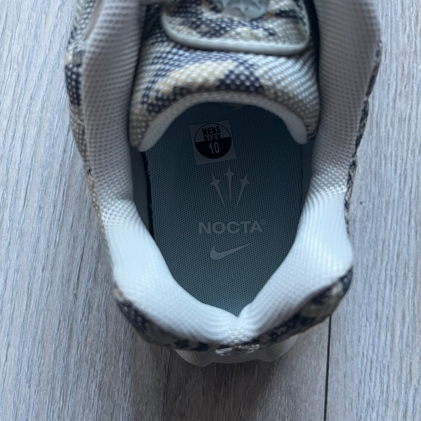 The Nike x NOCTA Hot Step Air Terra “Snakeskin” Light Bone Sneakers feature a low-top silhouette with a textured faux snakeskin upper in Light Bone tones mixed with cobblestone and gum light brown accents. The shoe includes small Swoosh logos on the sides, NOCTA three-star branding on the tongue, perforated quarter panels, and a metallic heel tag with Gore-Tex embossing. Finished with a white midsole housing a visible Air unit at the heel and a gum rubber outsole, style code DR0508-001, colorway Light Bone/