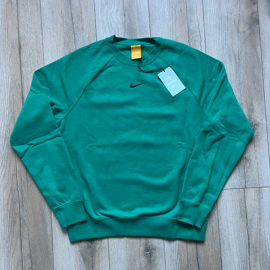 Nike x NOCTA Fleece “Neptune Green” Crewneck Sweatshirt FN8160-370 is a men’s pullover from the Cardinal Stock collection, finished in a Neptune Green/Black colorway. It features a regular fit with a round neckline, long sleeves, elastic cuffs, and an elasticated lower hem.&nbsp;Made from 82% cotton and 18% polyester fleece, the sweatshirt includes a silicone Swoosh logo and signature NOCTA branding, along with a back print, sleeve print, and 3D logo detailing. Made in Vietnam.