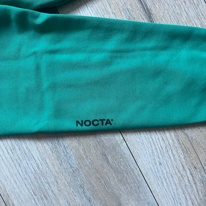 Nike x NOCTA Fleece “Neptune Green” Crewneck Sweatshirt FN8160-370 is a men’s pullover from the Cardinal Stock collection, finished in a Neptune Green/Black colorway. It features a regular fit with a round neckline, long sleeves, elastic cuffs, and an elasticated lower hem.&nbsp;Made from 82% cotton and 18% polyester fleece, the sweatshirt includes a silicone Swoosh logo and signature NOCTA branding, along with a back print, sleeve print, and 3D logo detailing. Made in Vietnam.