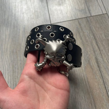 Oakley 2004 Black Leather Skull Belt is a genuine black leather belt featuring full-length holes for adjustable sizing. The belt end is embossed with a carved Oakley logo, and it includes a metal skull buckle with Oakley branding. Made in 2004, it combines durable leather construction with signature Oakley design details.