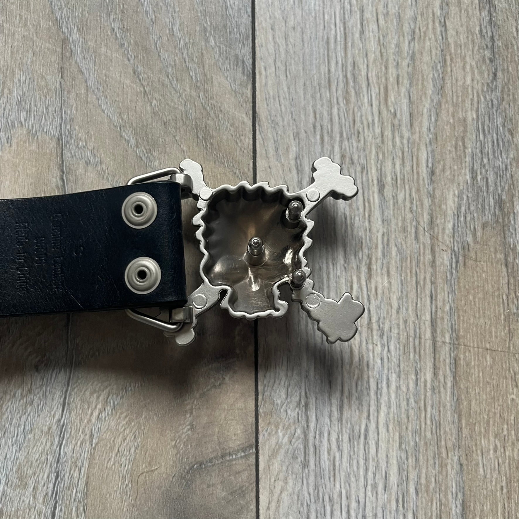 Oakley 2004 Black Leather Skull Belt is a genuine black leather belt featuring full-length holes for adjustable sizing. The belt end is embossed with a carved Oakley logo, and it includes a metal skull buckle with Oakley branding. Made in 2004, it combines durable leather construction with signature Oakley design details.