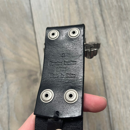 Oakley 2004 Black Leather Skull Belt is a genuine black leather belt featuring full-length holes for adjustable sizing. The belt end is embossed with a carved Oakley logo, and it includes a metal skull buckle with Oakley branding. Made in 2004, it combines durable leather construction with signature Oakley design details.