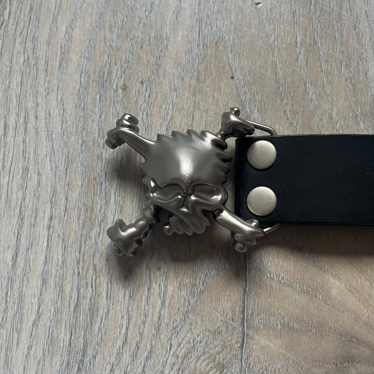 Oakley 2004 Black Leather Skull Belt is a genuine black leather belt featuring full-length holes for adjustable sizing. The belt end is embossed with a carved Oakley logo, and it includes a metal skull buckle with Oakley branding. Made in 2004, it combines durable leather construction with signature Oakley design details.