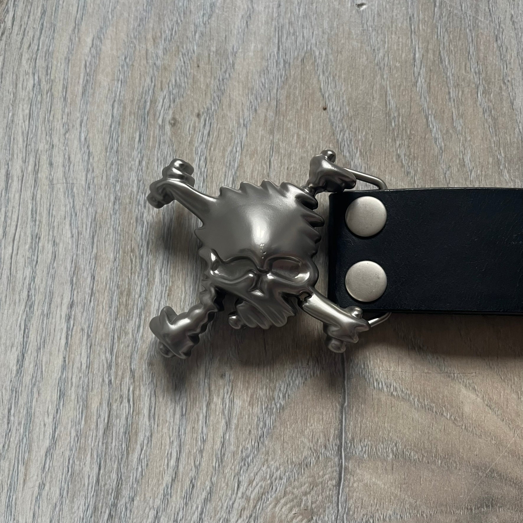 Oakley 2004 Black Leather Skull Belt is a genuine black leather belt featuring full-length holes for adjustable sizing. The belt end is embossed with a carved Oakley logo, and it includes a metal skull buckle with Oakley branding. Made in 2004, it combines durable leather construction with signature Oakley design details.