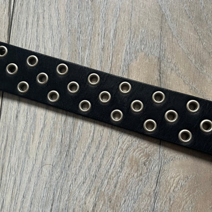 Oakley 2004 Black Leather Skull Belt is a genuine black leather belt featuring full-length holes for adjustable sizing. The belt end is embossed with a carved Oakley logo, and it includes a metal skull buckle with Oakley branding. Made in 2004, it combines durable leather construction with signature Oakley design details.