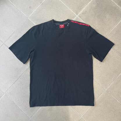 Oakley 2000's Metal Ellipse Black Tee is a black T-shirt made from 95% cotton and 5% spandex, featuring a raised collar with a metal Oakley Ellipse logo and a red stripe printed with Oakley logos on one shoulder.