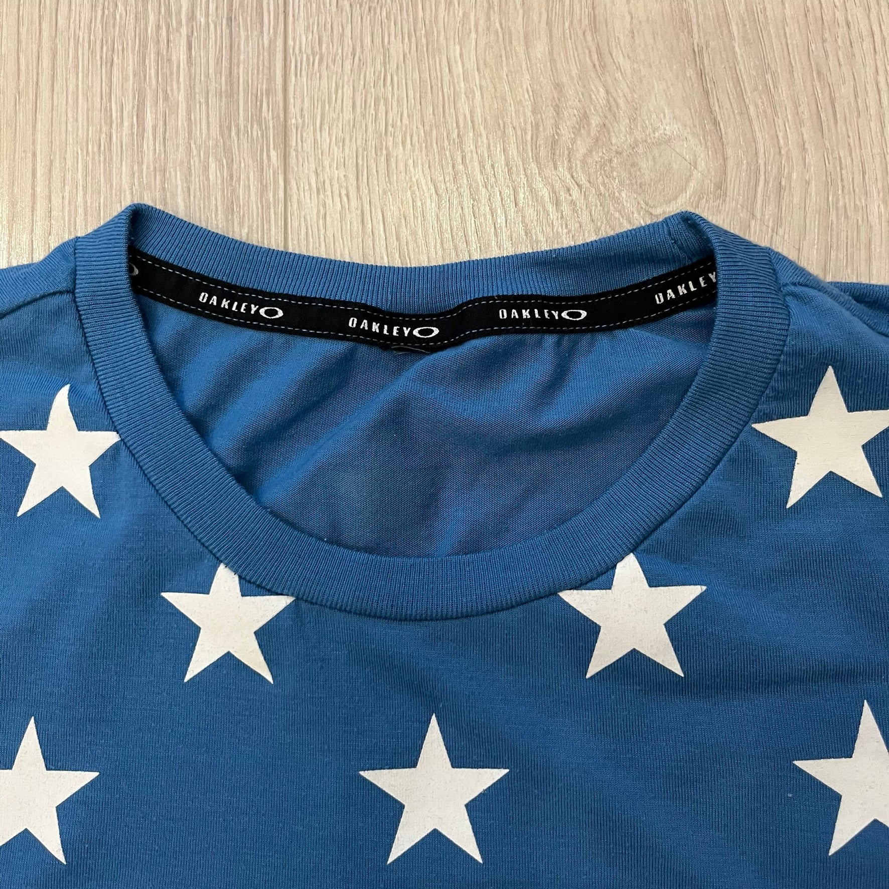 Oakley Crazy Stars Tee in blue with an all-over white star print covering the top two-thirds of the front, back, and sleeves. Features a large Oakley “O” logo on the front. Made from a cotton/polyester blend in El Salvador.