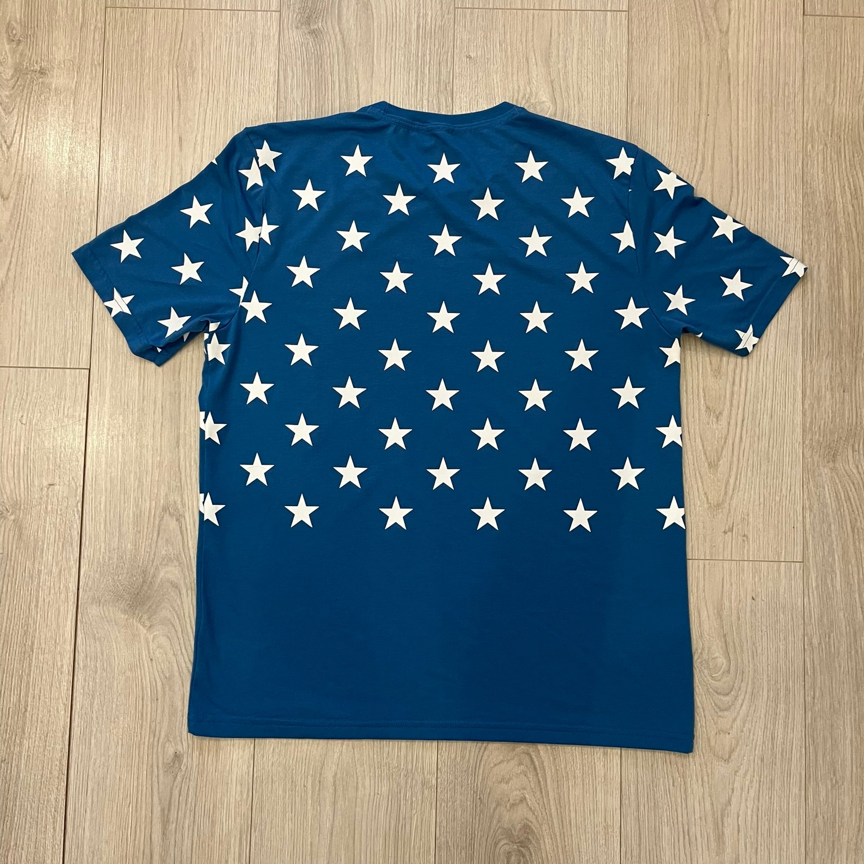 Oakley Crazy Stars Tee in blue with an all-over white star print covering the top two-thirds of the front, back, and sleeves. Features a large Oakley “O” logo on the front. Made from a cotton/polyester blend in El Salvador.