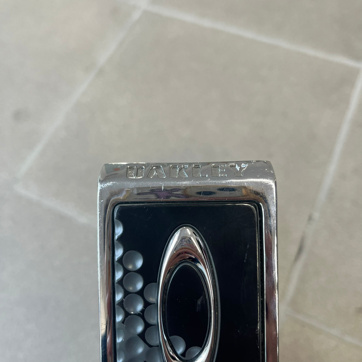 Oakley Ellipse 2010's Gray Leather Belt features a gray leather strap with a cut-to-size construction for adjustable length. The metal rectangular buckle has a silver outer frame, black center insert, and a silver Oakley Ellipse logo in the middle, with an engraved Oakley logo on the side.