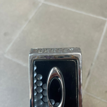 Oakley Ellipse 2010's Gray Leather Belt features a gray leather strap with a cut-to-size construction for adjustable length. The metal rectangular buckle has a silver outer frame, black center insert, and a silver Oakley Ellipse logo in the middle, with an engraved Oakley logo on the side.