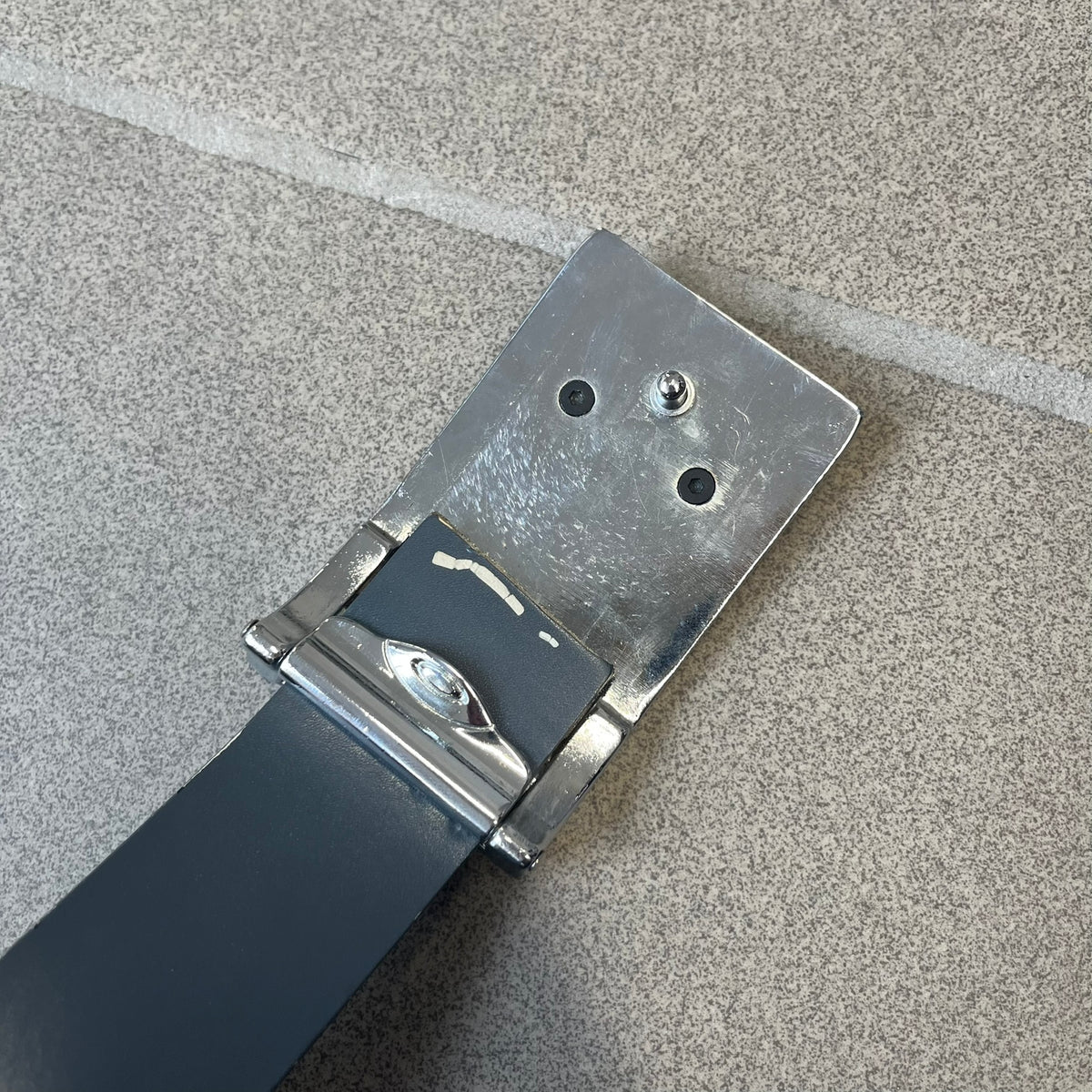 Oakley Ellipse 2010's Gray Leather Belt features a gray leather strap with a cut-to-size construction for adjustable length. The metal rectangular buckle has a silver outer frame, black center insert, and a silver Oakley Ellipse logo in the middle, with an engraved Oakley logo on the side.