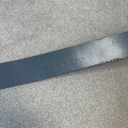 Oakley Ellipse 2010's Gray Leather Belt features a gray leather strap with a cut-to-size construction for adjustable length. The metal rectangular buckle has a silver outer frame, black center insert, and a silver Oakley Ellipse logo in the middle, with an engraved Oakley logo on the side.