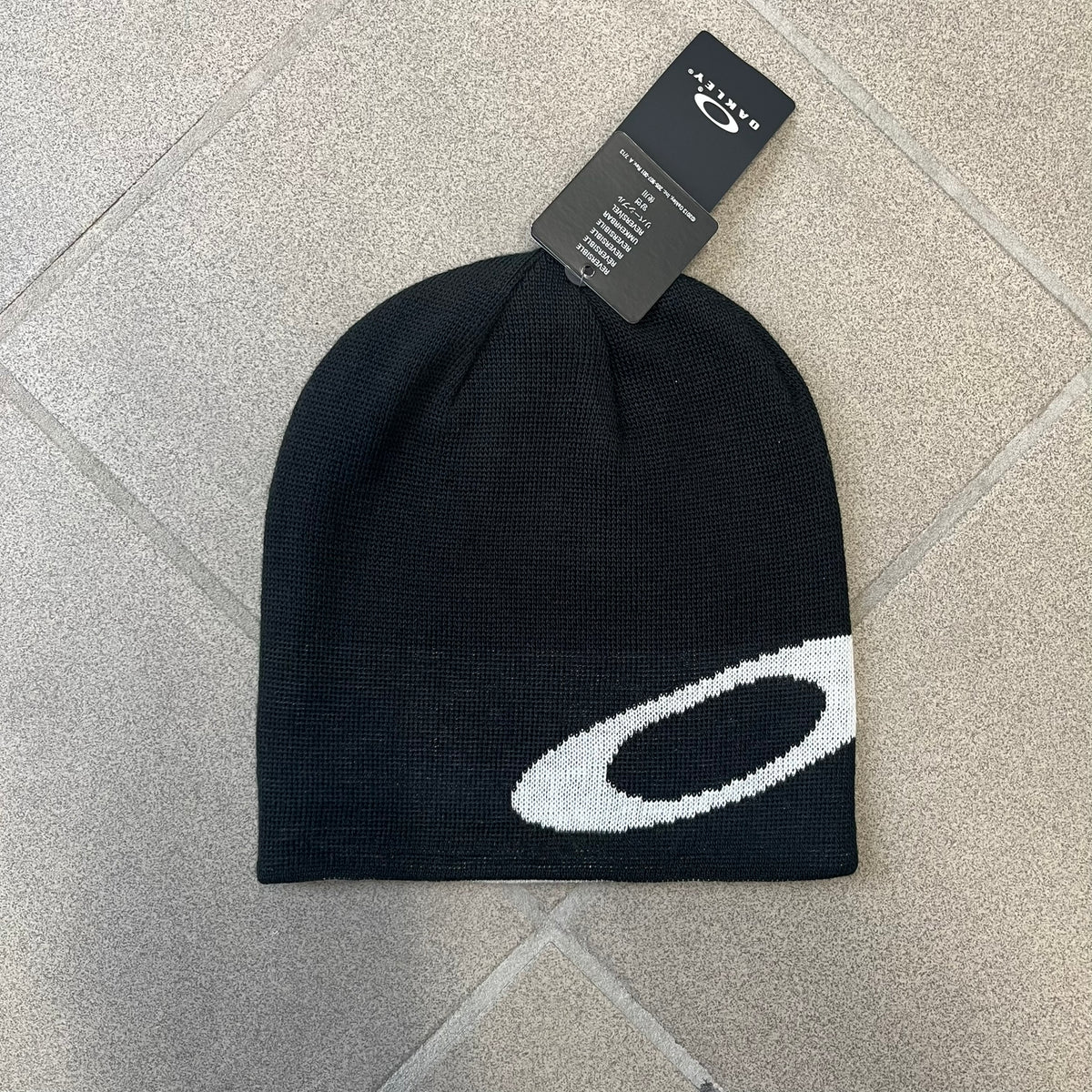 Oakley Ellipse Black Side Beanie is a classic-fit, fine-knit beanie made from 100% acrylic, with a reversible two-sided build. It has a contrasting white jacquard Oakley Ellipse logo on the side and a small logo flag. Designed for casual wear and outdoor performance with reliable warmth and fit.