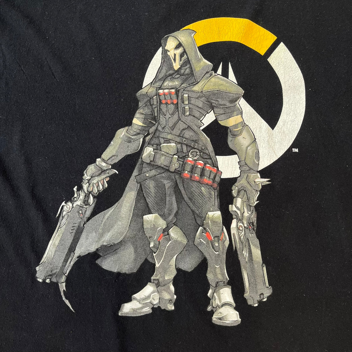 Overwatch 2017 Reaper Black Tee features a black construction with a full-color graphic of Reaper standing with his guns in front of the Overwatch logo, with a small “TM” mark beside it. Finished with a licensed 2017 Overwatch Gaya neck tag.
