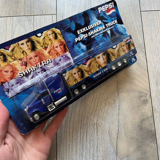Pepsi 2000’s Shakira 1:87 Delivery Truck Model is a limited edition promotional model featuring a blue Pepsi delivery truck covered with graphics of Shakira alongside Pepsi logos and name text. The model remains in its original clear plastic display case attached to a printed cardboard backing with Pepsi and Shakira branding. This German edition promotional piece was produced as part of early 2000s Pepsi marketing campaigns.