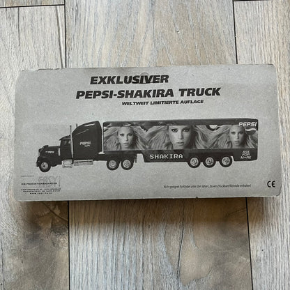 Pepsi 2000’s Shakira 1:87 Delivery Truck Model is a limited edition promotional model featuring a blue Pepsi delivery truck covered with graphics of Shakira alongside Pepsi logos and name text. The model remains in its original clear plastic display case attached to a printed cardboard backing with Pepsi and Shakira branding. This German edition promotional piece was produced as part of early 2000s Pepsi marketing campaigns.