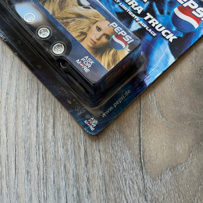 Pepsi 2000’s Shakira 1:87 Delivery Truck Model is a limited edition promotional model featuring a blue Pepsi delivery truck covered with graphics of Shakira alongside Pepsi logos and name text. The model remains in its original clear plastic display case attached to a printed cardboard backing with Pepsi and Shakira branding. This German edition promotional piece was produced as part of early 2000s Pepsi marketing campaigns.