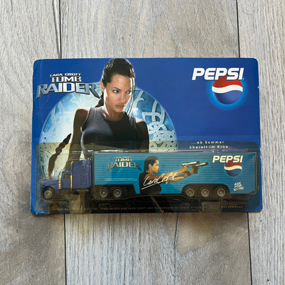 Pepsi 2001 Lara Croft Tomb Raider 1:87 Delivery Truck Model is a promotional die-cast style truck released alongside the film Lara Croft: Tomb Raider. The model features a blue Pepsi delivery truck with a large graphic of Lara Croft and Pepsi branding on the sides. It comes displayed in a clear plastic case attached to a printed cardboard backing with Tomb Raider and Pepsi graphics. The bottom of the case includes 2001 Paramount Pictures licensing.