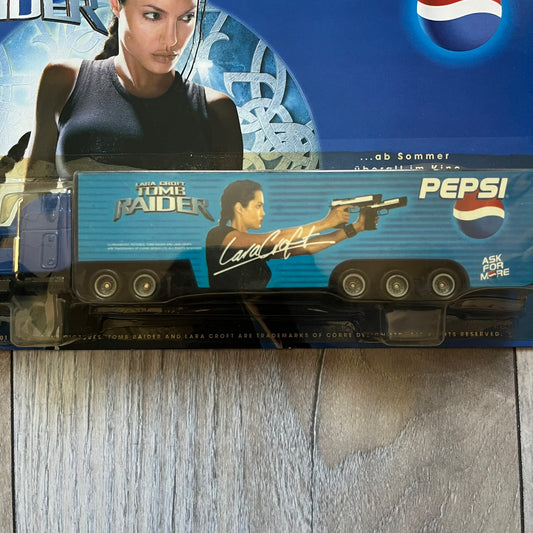 Pepsi 2001 Lara Croft Tomb Raider 1:87 Delivery Truck Model is a promotional die-cast style truck released alongside the film Lara Croft: Tomb Raider. The model features a blue Pepsi delivery truck with a large graphic of Lara Croft and Pepsi branding on the sides. It comes displayed in a clear plastic case attached to a printed cardboard backing with Tomb Raider and Pepsi graphics. The bottom of the case includes 2001 Paramount Pictures licensing.