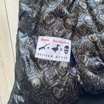 Philipp Plein 2010's Black Waxed Puffer Jacket is a black puffer jacket with a removable fur-trimmed hood attached by zipper. The jacket features heavy silver-tone hardware throughout, including large zipper pulls shaped as crosses with a skull in the center. The right chest has a crystal “P” patch set, while the left chest features two zip pockets. The hood drawstrings are finished with silver skull tips marked with a “P.”

One shoulder is finished with metal Philipp Plein logo plaque. The interior lining 