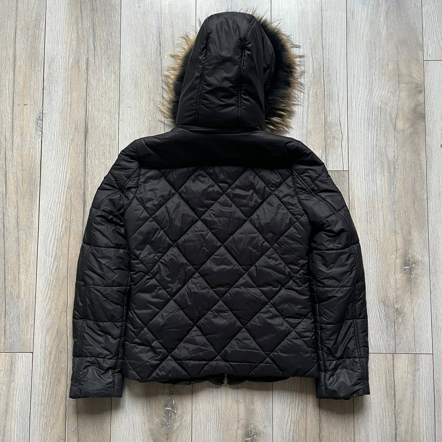 Philipp Plein 2010's Fur Hood Puffer Jacket is a black puffer jacket with a removable fur-trimmed hood attached by zipper. The jacket features heavy silver-tone hardware throughout, including 3 large zipper pulls used on the front pockets, main zipper and one drawstring ending. The right arm has a black “P” patch set with crystals.