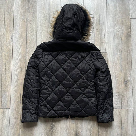 Philipp Plein 2010's Fur Hood Puffer Jacket is a black puffer jacket with a removable fur-trimmed hood attached by zipper. The jacket features heavy silver-tone hardware throughout, including 3 large zipper pulls used on the front pockets, main zipper and one drawstring ending. The right arm has a black “P” patch set with crystals.