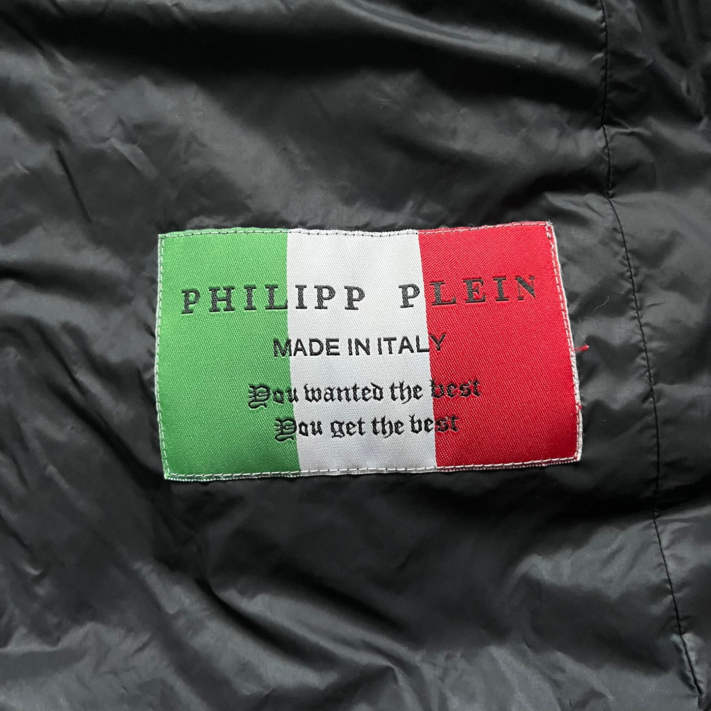Philipp Plein 2010's Fur Hood Puffer Jacket is a black puffer jacket with a removable fur-trimmed hood attached by zipper. The jacket features heavy silver-tone hardware throughout, including 3 large zipper pulls used on the front pockets, main zipper and one drawstring ending. The right arm has a black “P” patch set with crystals.