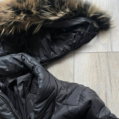 Philipp Plein 2010's Fur Hood Puffer Jacket is a black puffer jacket with a removable fur-trimmed hood attached by zipper. The jacket features heavy silver-tone hardware throughout, including 3 large zipper pulls used on the front pockets, main zipper and one drawstring ending. The right arm has a black “P” patch set with crystals.