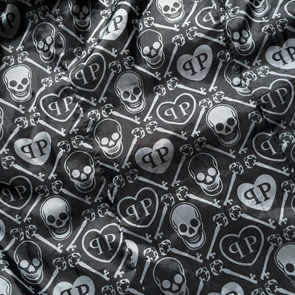 Philipp Plein 2010's No Hood Puffer Jacket is a black puffer jacket, with silver-tone hardware throughout including large zipper pulls shaped as crosses with a skull in the center used on the pockets, buttons with PP Skulls and metal "spikes" on the shoulders. The right arm has a white/clear “P” patch set with crystals. The interior lining has an all-over print featuring keys, skulls, and PP logos.